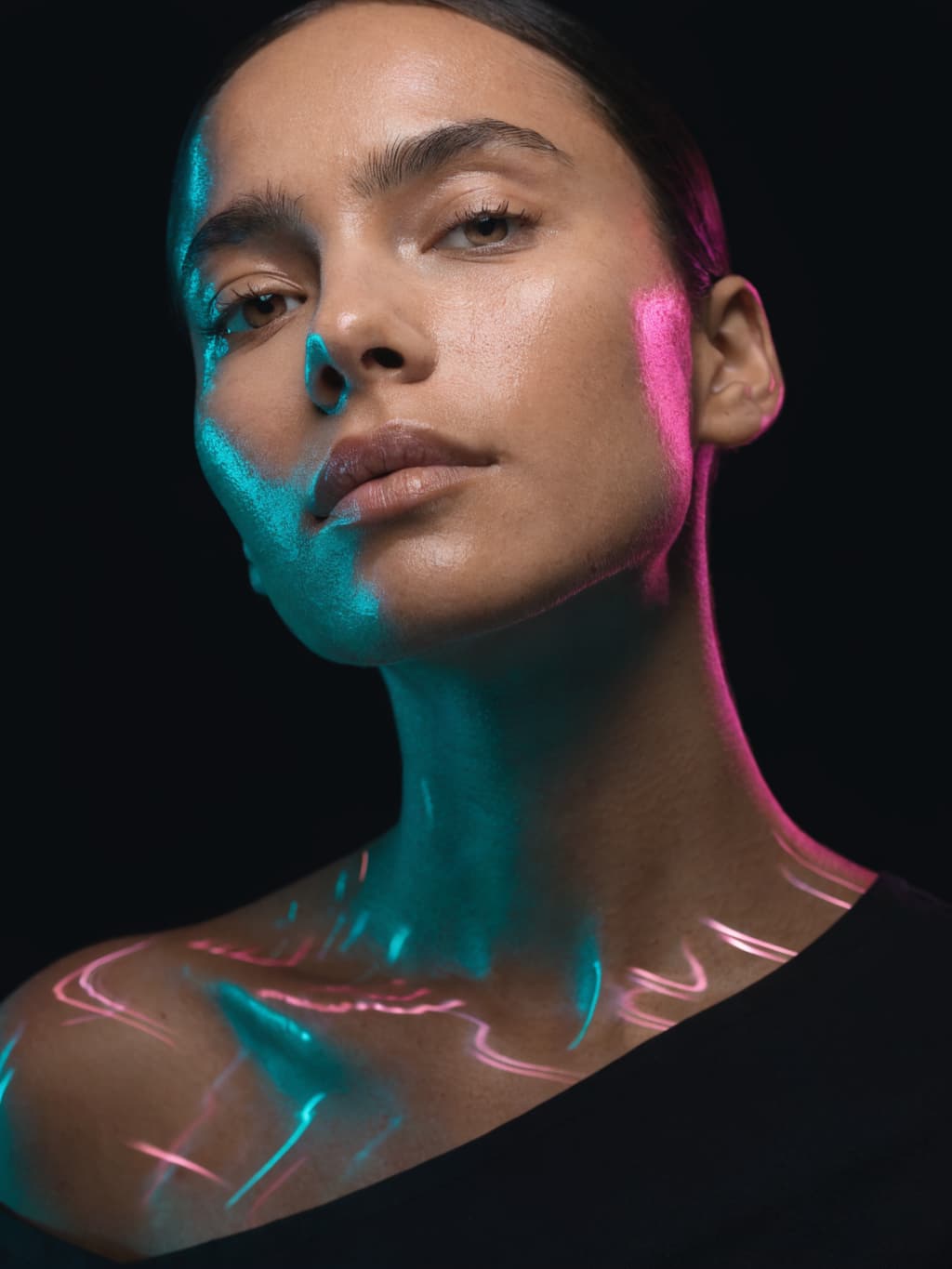 A close-up portrait of a woman illuminated by vibrant blue and pink neon lighting against a dark background.